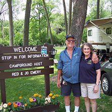 campground hosts standing next to camping sign with RV in background