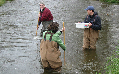 A group of people wearing waders in a stream collecting water samples