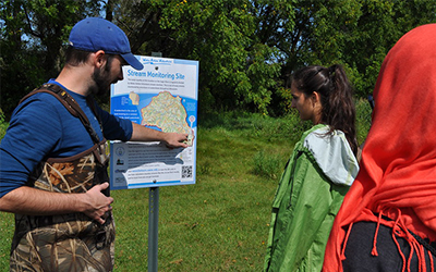 A group of people looking at a stream monitoring site sign