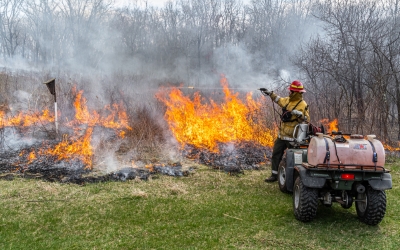 burn boss using a water ATV to spray down a wooden bird house within a prairie burn