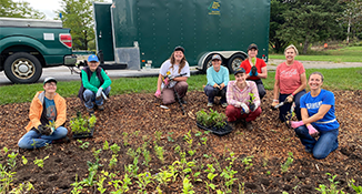 A group of people crouching down for a photo on a mulched area with small green plants planted in it