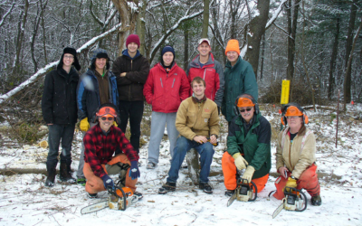 A group of youth and adults (with chainsaws) posing for a picture in the snow following an invasive species removal workday