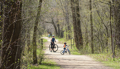 Adult and child biking on a crushed limestone path through the forest at CamRock County Park
