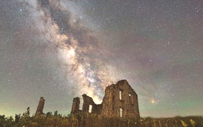 Matz stone house remnants with grass in foreground, under a vivid Milky Way night sky.