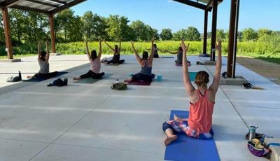 People sitting on yoga mats under the solar shelter doing a yoga pose