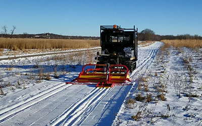 large piece of equipment laying tracks on a snowy trail