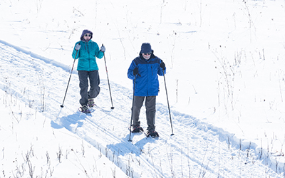 Two people bundled up skiing on a snowy trail.