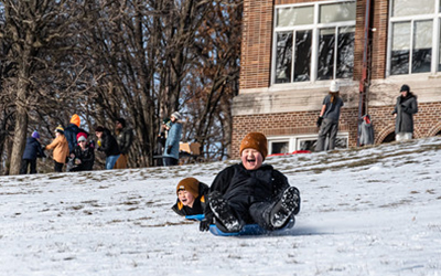Children sledding down a snowy hill with expressions of joy on their faces