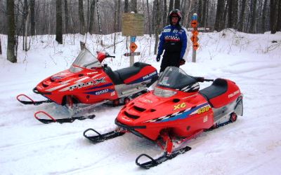 snowmobiler standing behind two snowmobiles