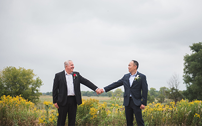 A couple holding hands in a prairie filled with yellow flowers.